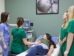 Student practicing a sonogram on another student with two other students and the instructor observing