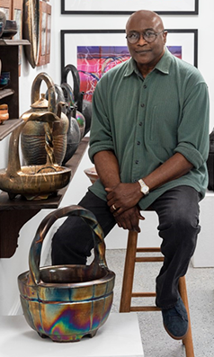 sJames Watkins seated in front of his ceramic work