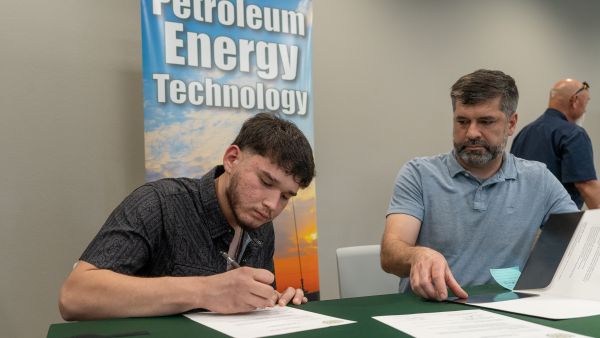 smale high school senior student signs a commitment letter at a midland college table next to the department chair of the energy technology program.