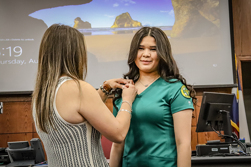 The image to use for this article. Listing image managed through RSS tab. Janie Enriques, Certified Nurse Aide graduate, is pinned by Instructor Erika Ortiz, LVN