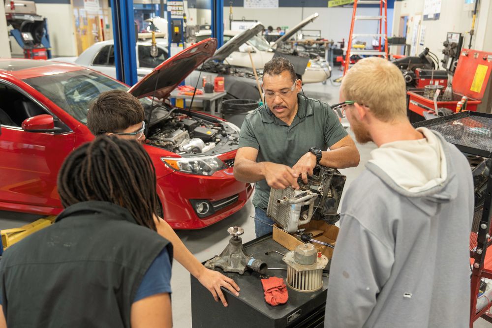 sstudents gather in MC's automotive lab to listen to professor demonstrate repair technique on automotive equipment