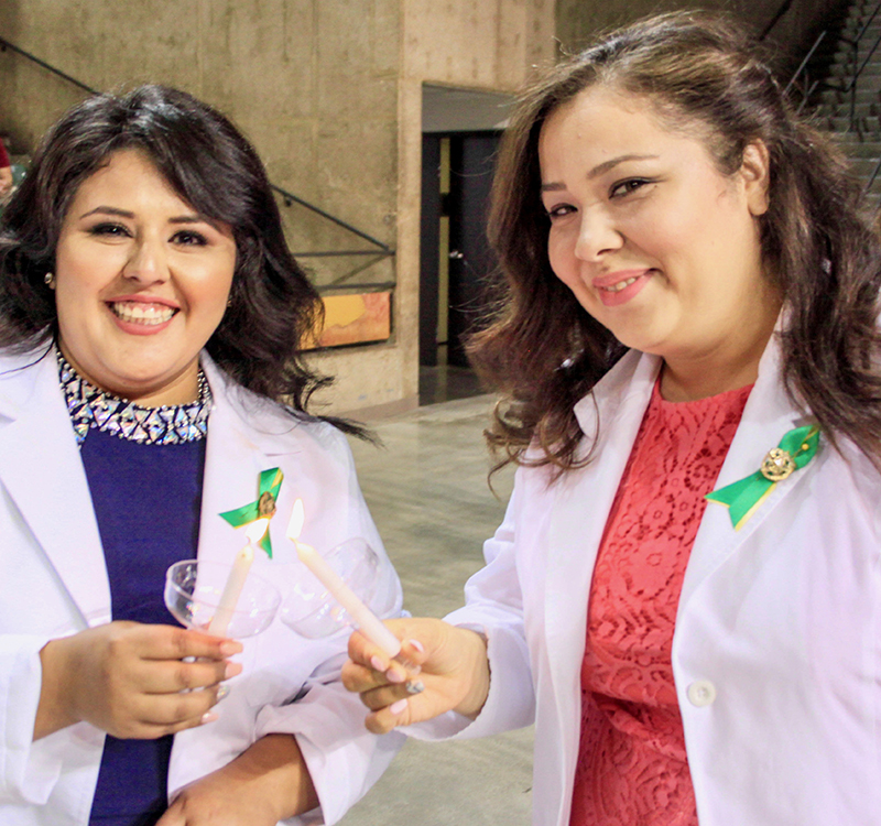 sJasmine Lopez and Lenora Munoz light candles during the May 8 Associate Degree Nurse Pinning Ceremony