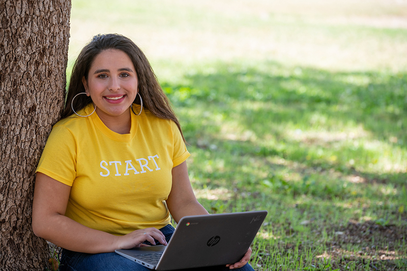 The image to use for this article. Listing image managed through RSS tab. Female sitting under tree with laptop wearing "Start" t-shirt.