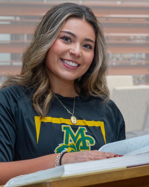 The image to use for this article. Listing image managed through RSS tab. MC student poses in front of dictionary with a title of offering tips to succeed in an 8-week course.
