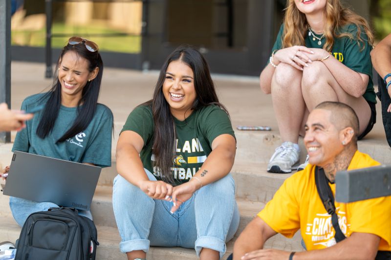 sfour MC students from different backgrounds sit on the steps of the Learning Resource Center smiling for the camera
