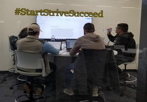 Students sitting at the table looking at the big screen on the wall